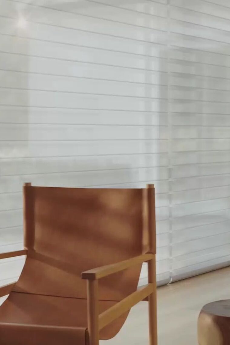 A hand holding a remote as a motorized linen roller shade descends a tall window