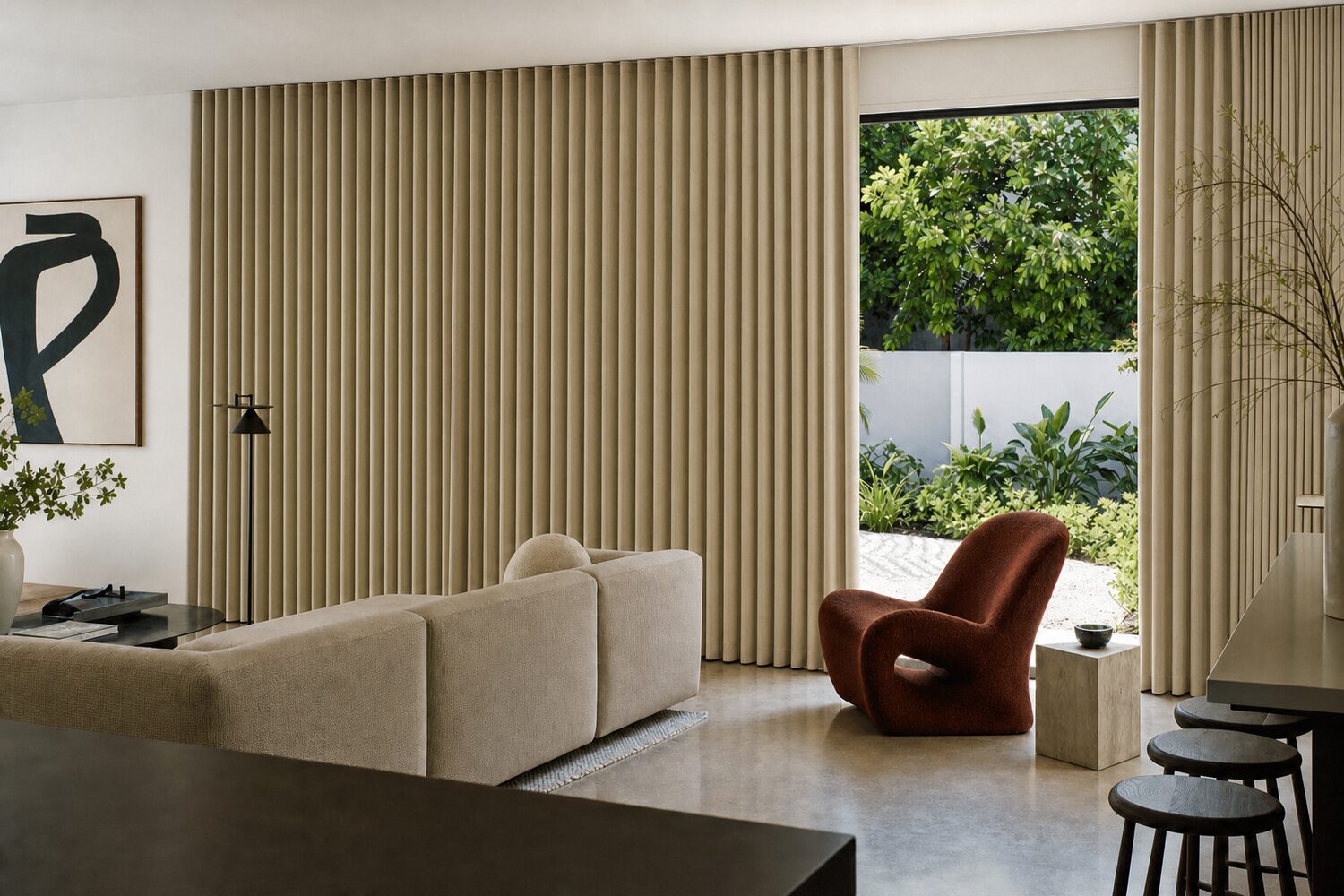 An open-plan living space with a long low sofa and polished concrete floor, oatmeal ripple-fold drapery running wall to wall across sliding doors with one section drawn back