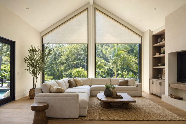 A cathedral-ceilinged living room with a glazed gable end, two windows rising to the ridge each fitted with a shade cut to its own rake