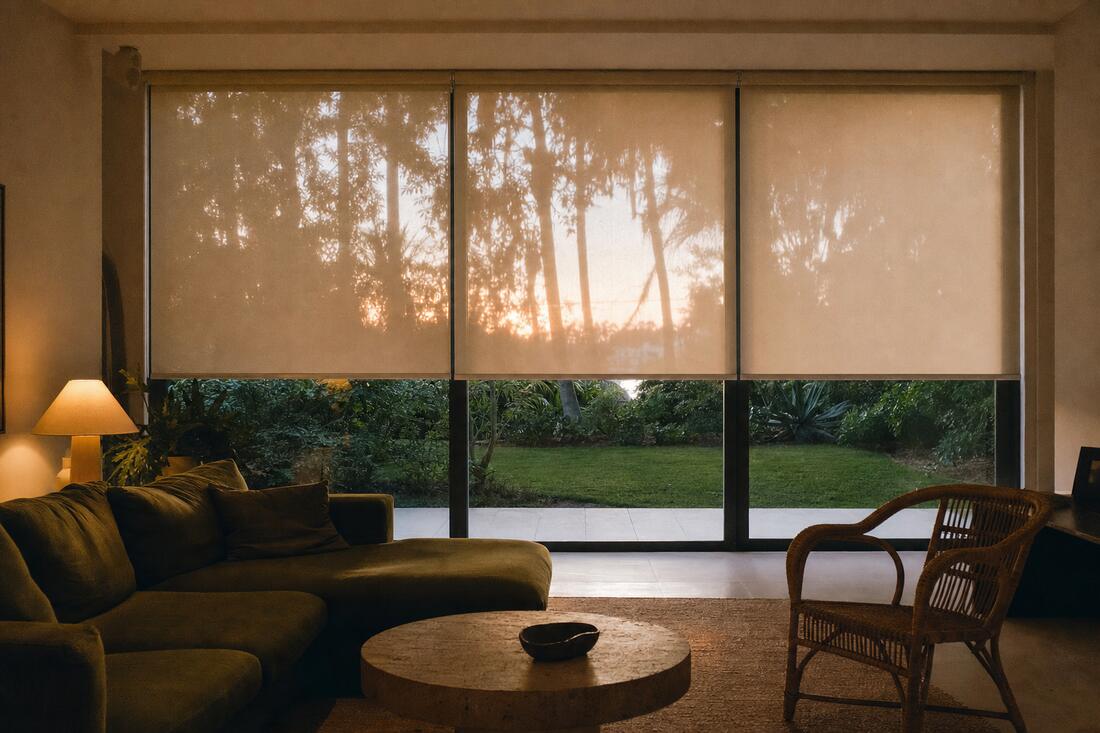 Three motorized flax shades across a wall of sliding doors at dusk, all stopped at the same height with one lamp lit inside