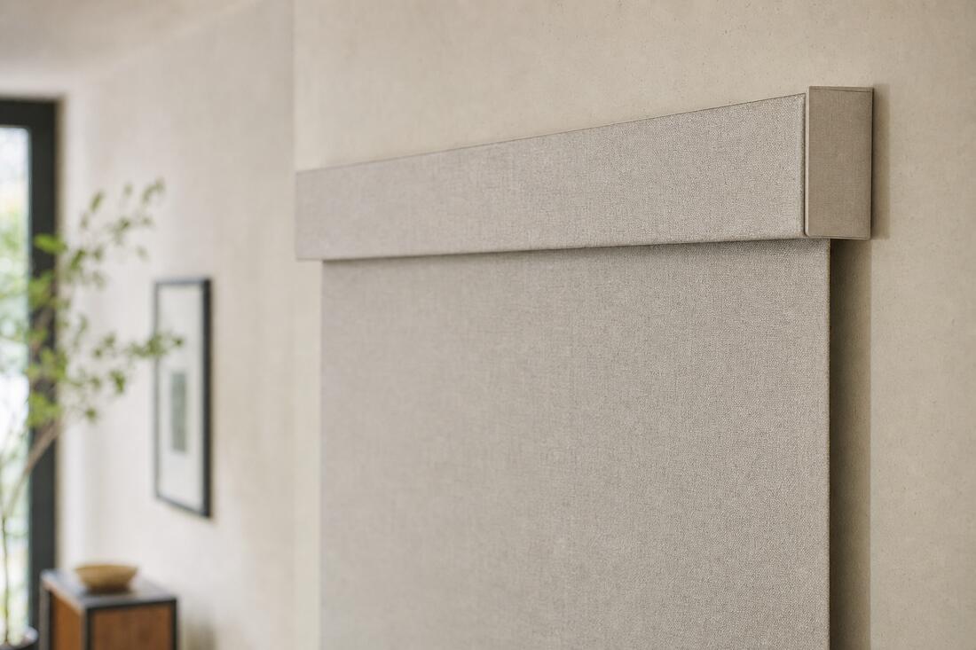 A close view of a fabric-wrapped cassette at the head of a window, the oatmeal linen dropping from it in one smooth plane