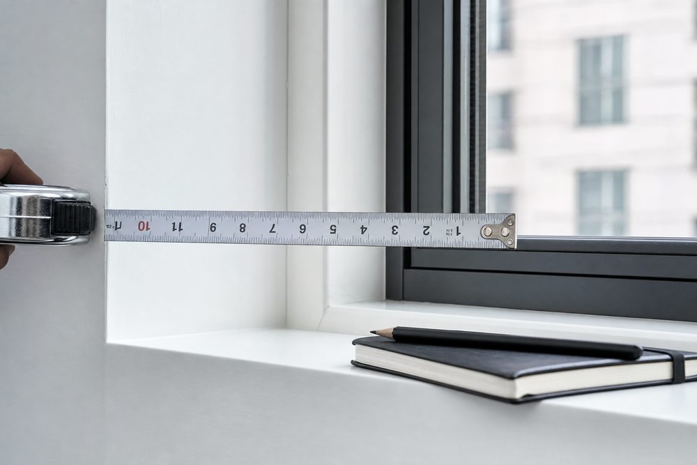 A steel tape measure extended across a white window recess beside a notebook